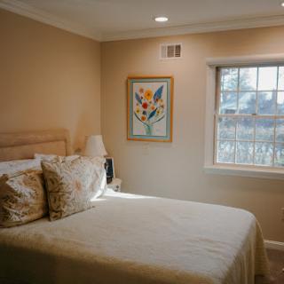 A cozy and softly lit bedroom featuring a neatly made bed, decorative pillows, and a window with a view.