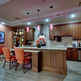 A modern kitchen with wooden cabinets and an island, featuring pendant lights and vibrant chairs.