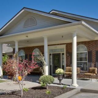 A residential house with a covered porch and white columns, surrounded by landscaping.