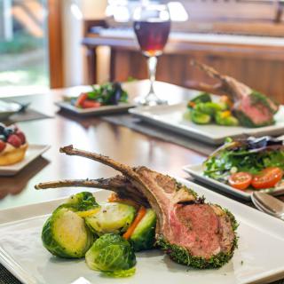 A gourmet meal featuring herb-crusted lamb chops and Brussels sprouts, accompanied by a glass of wine.