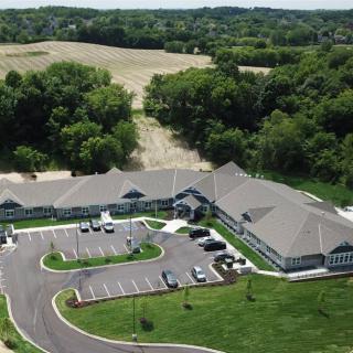 An aerial view of a building with an adjacent parking lot set in a rural landscape surrounded by trees.