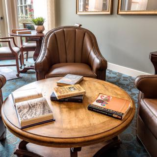 A cozy reading area with books on a round wooden table surrounded by leather chairs.