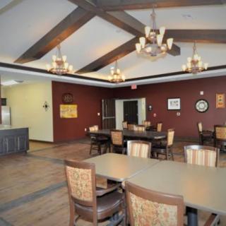 A spacious dining area with wooden tables, chairs, and elegant chandeliers beneath a beamed ceiling.