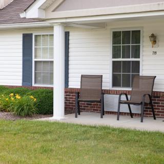 A cozy front porch with two chairs and a window, surrounded by a well-kept yard.