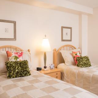 A cozy bedroom featuring twin beds with decorative pillows, a bedside lamp, and framed artwork on the walls.
