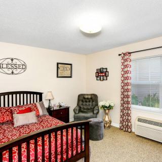 A cozy bedroom with a red and black patterned bedspread, a comfortable armchair, and decorative accents.