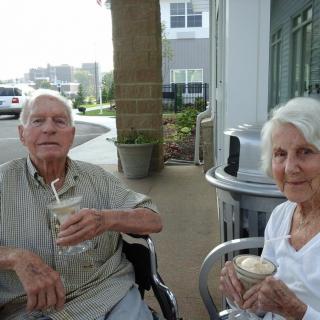 An elderly couple enjoying drinks while sitting outside.
