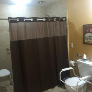 An accessible bathroom with a shower curtain, toilet, and supportive handrails.