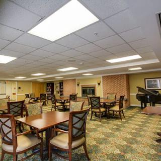 A spacious interior room featuring multiple tables and chairs, a piano, and well-lit surroundings.