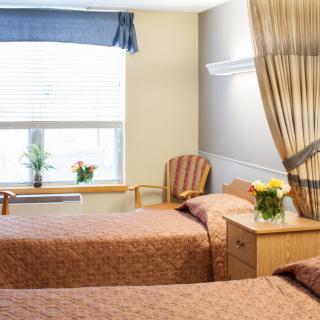 A hospital room with two neatly made beds, separated by a curtain, and a window letting in natural light.