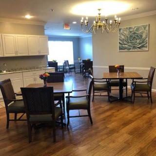 A spacious dining area with wooden flooring, multiple tables and chairs, and a chandelier.
