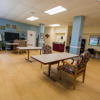 A spacious community lounge area featuring tables and colorful chairs.