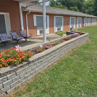 Brick building with a patio, chairs, and landscaped flower bed.