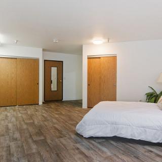 A spacious minimalist bedroom with wooden floors and white bedding, featuring closet doors and a mirror.