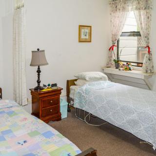 A cozy bedroom featuring two twin beds, a nightstand with a lamp, and a window with floral curtains.