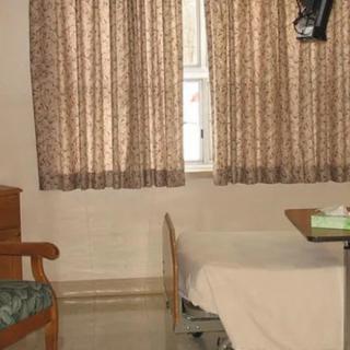 A simple hospital room with a bed, chair, and patterned curtains.