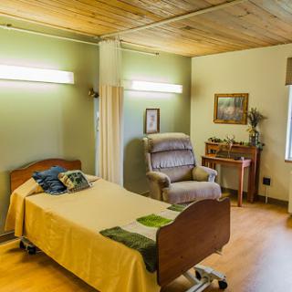 A serene hospital room featuring a single bed, a comfortable chair, and warm lighting.