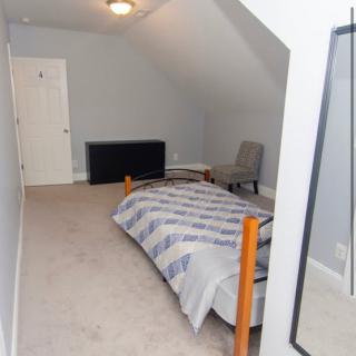 A minimalist attic bedroom with a single bed and chair.