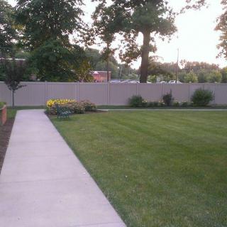 A well-maintained lawn with a concrete pathway and surrounding trees.