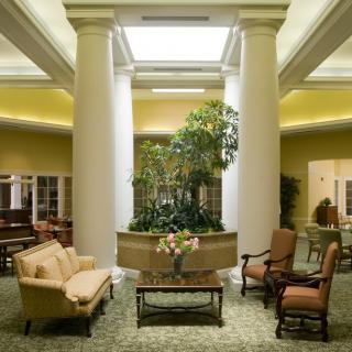 A well-lit lobby featuring elegant furniture, large pillars, and greenery.