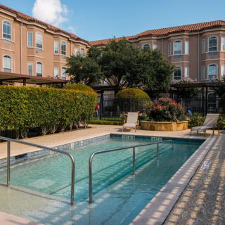 A serene outdoor pool area surrounded by lush greenery and a brick building.