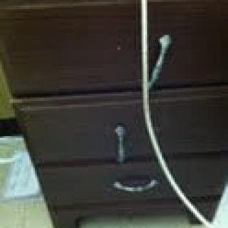A brown wooden drawer with metal handles and a cable draped over it.