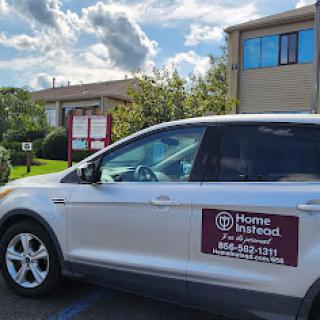 A vehicle with an advertisement for home services parked in front of a building under a partly cloudy sky.