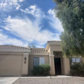 A single-story house with desert landscaping under a blue sky with clouds.