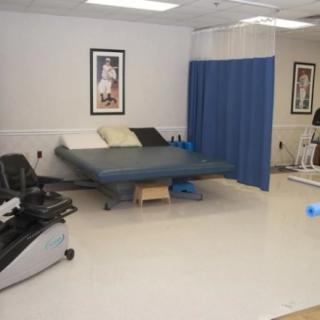 A physical therapy room equipped with an exercise bike, a therapy bed, and a blue privacy curtain.