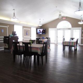 A bright dining area with wooden floors, multiple tables and chairs, and a television mounted on the wall.