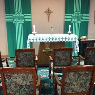 A small chapel with an altar adorned with candles and a cross, surrounded by chairs for worship.