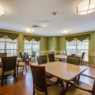 A well-lit dining room with multiple tables and chairs, featuring green walls and large windows.