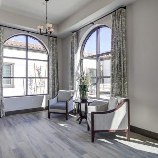A bright and elegant living space featuring large arched windows, stylish chairs, and chic curtains.