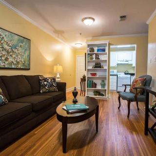 A cozy living room with a dark sofa and a wooden coffee table, leading to a kitchen through a bookshelf partition.