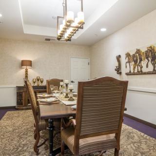 A beautifully decorated dining room with a large table and elegant chairs, featuring artwork on the walls and warm lighting.