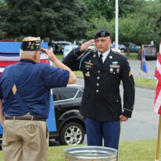 A serviceman in uniform salutes a veteran during an outdoor ceremony.