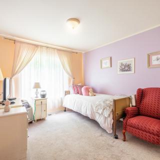 A cozy bedroom with a single bed and purple walls, complemented by an armchair and soft natural lighting.