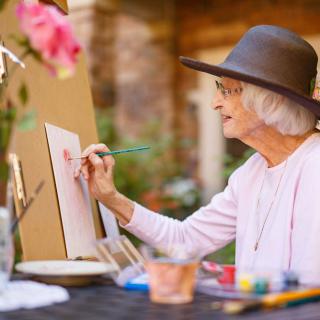 An elderly woman painting outdoors, showcasing her artistic creativity.