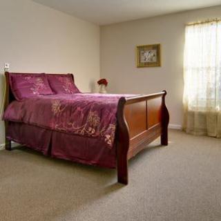 A cozy bedroom featuring a wooden bed with purple bedding and a window allowing natural light.