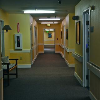 A dimly lit hospital hallway with yellow walls and several doors on either side.