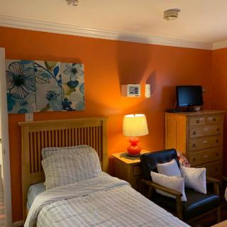 A cozy bedroom with an orange accent wall, featuring a single bed, wooden furniture, and decorative artwork.
