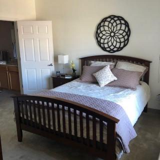 A cozy bedroom with a neatly made bed, decorative wall art, and a nightstand with a lamp.