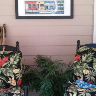 A cozy porch setup with two tropical-themed chairs and a vibrant painting on the wall.