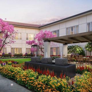 A beautifully landscaped courtyard featuring a central fountain, surrounded by vibrant flowers and trees.