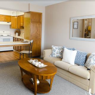 A cozy living room with an open view to the kitchen, featuring a beige sofa and a wooden coffee table.