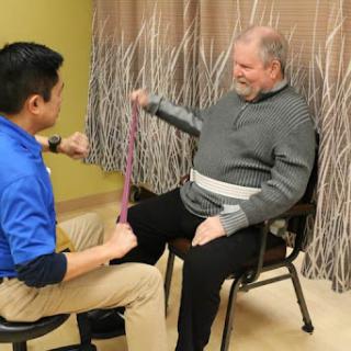 A therapist assists an elderly patient with a stretching exercise using resistance bands during a physical therapy session.