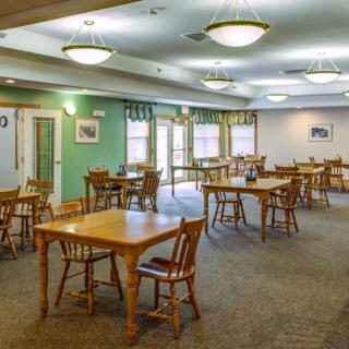 A spacious dining room with wooden tables and chairs, featuring soft lighting and a carpeted floor.