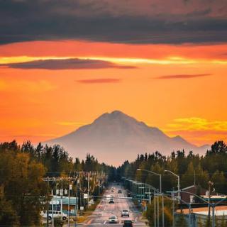 A serene view of a mountain at sunset, framed by a quiet road and lined with trees.