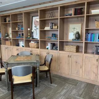 A cozy workspace featuring a wooden table surrounded by chairs and a neatly organized bookshelf.