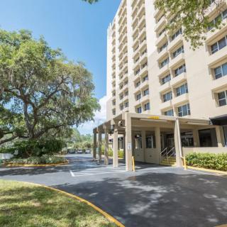 A high-rise apartment building with a driveway and surrounding trees.